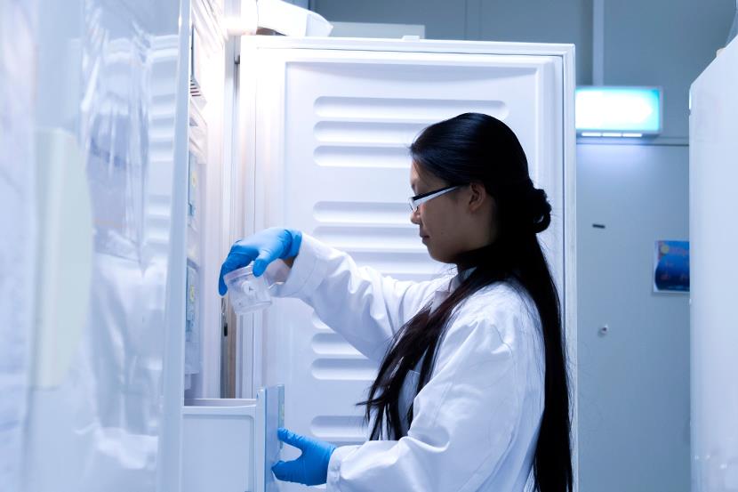 woman in white lab coat pulling samples from laboratory refrigerator