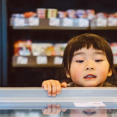 little girl peering over the edge and looking into a freezer chest at a supermarket