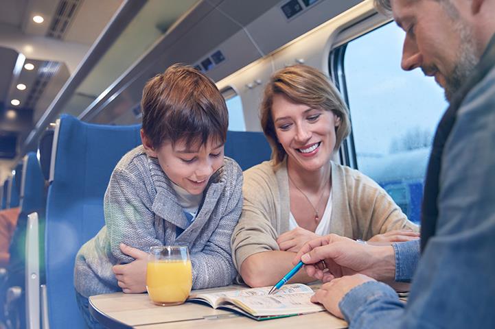 sitting man woman and child looking at a book on a passenger train