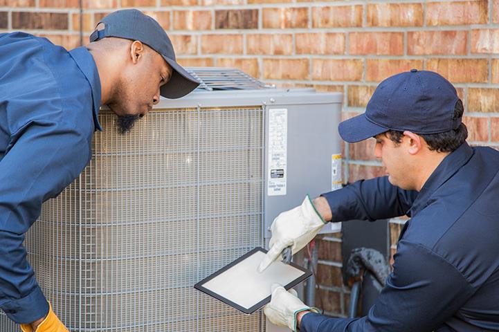 two men net to exterior air conditioning heat pump system one man holding a tablet and the other man